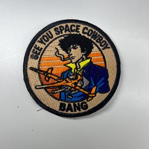 May include: Circular embroidered patch featuring a character from Cowboy Bebop. The character is depicted with a cigarette, holding a gun, and wearing a blue jacket. The text "SEE YOU SPACE COWBOY" and "BANG" are included.