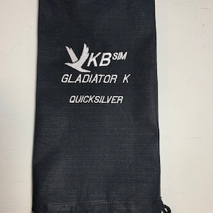 Könnte beinhalten: Schwarze Kordelzugtasche mit weißer Stickerei. Die Stickerei enthält einen stilisierten Vogel, den Text "KB SIM", "GLADIATOR K" und "QUICKSILVER".