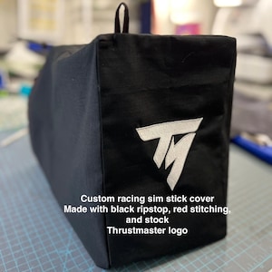 Peut inclure: Housse de protection noire personnalisée pour manette de simulation de course avec logo Thrustmaster blanc. Fabriquée en tissu ripstop noir et coutures rouges. Boucle noire sur le dessus.