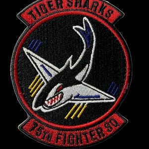 May include: A red, white, and blue embroidered patch with a black shark silhouette and the text "Tiger Sharks 15th Fighter Sq".