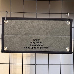 May include: A gray velcro patch display, 16" x 8", with a black fabric border. The display has four metal grommets and can hold up to 14 patches. The text on the display reads "16"x8" Gray velcro Black fabric Holds up to 14 patches."