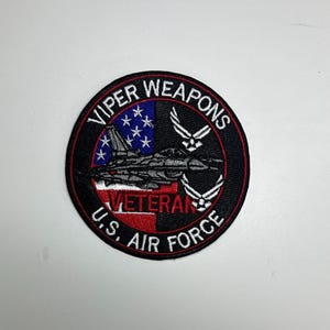 Puede incluir: Parche circular con borde negro. Presenta el texto "VIPER WEAPONS" y "U.S. AIR FORCE". Incluye una imagen de un avión a reacción, la bandera estadounidense y la palabra "VETERAN". También hay dos juegos de alas blancas.