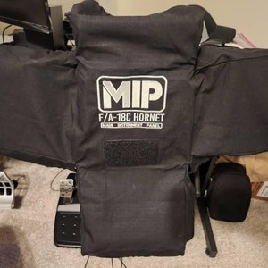 Könnte beinhalten: Schwarzes Stoffpaneel mit dem weißen Text "MIP F/A-18C HORNET MAIN INSTRUMENT PANEL". Das Paneel hat eine rechteckige Form mit angebrachten Seitenteilen. Ein schwarzer Klettverschluss ist auf der Vorderseite sichtbar.