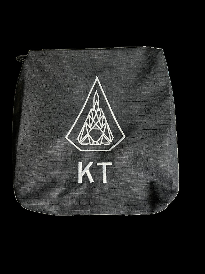 Puede incluir: Bolsa de lona negra con un dise&ntilde;o geom&eacute;trico blanco y las letras "KT" bordadas en la parte delantera.