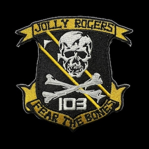 Op de afbeelding: Een geborduurde zwarte en gele patch met een schedel en gekruiste botten, de tekst "Jolly Rogers" en "Fear the Bones", en het nummer "103".