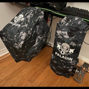 Puede incluir: Dos fundas de tela de camuflaje negro y gris con texto bordado en blanco y un logotipo de calavera. El texto en las fundas dice "PALADIN".
