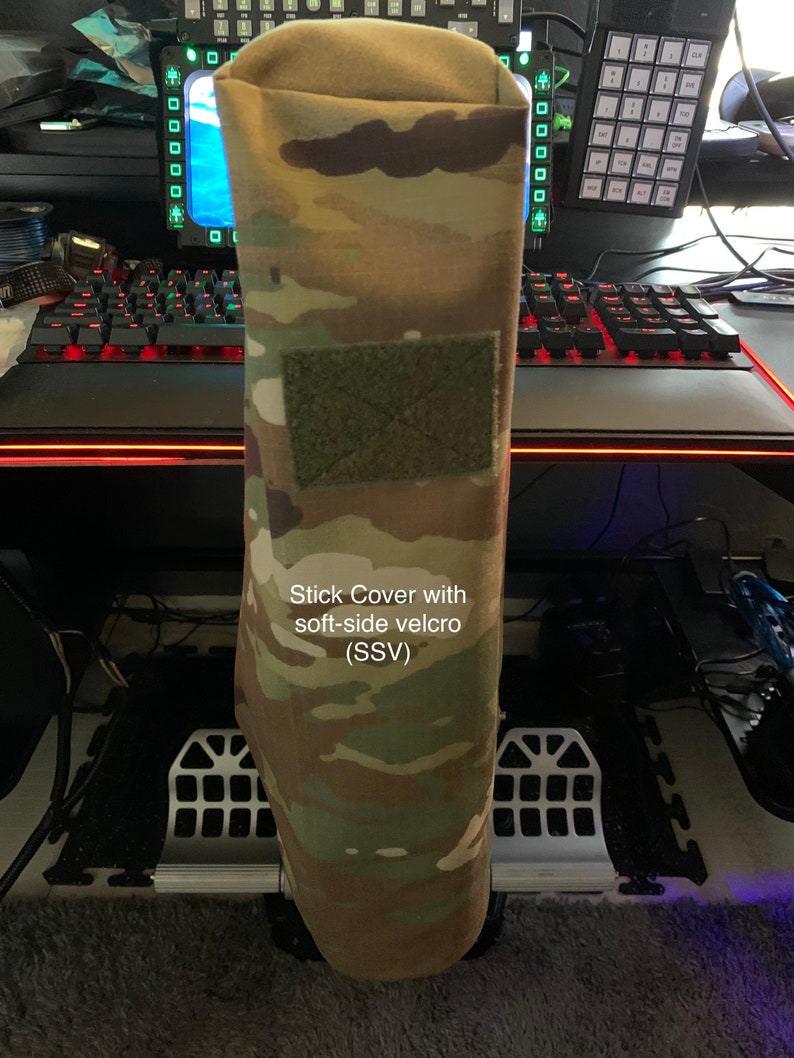 May include: A camouflage stick cover with soft-side velcro (SSV). The cover has a green velcro patch on the front.