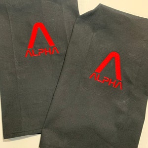 May include: Two black fabric kitchen towels with red embroidered logos. The logo is a stylised letter A with the word "ALPHA" underneath.