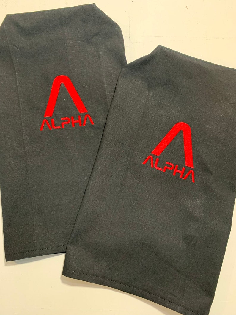 May include: Two black fabric kitchen towels with red embroidered logos. The logo is a stylised letter A with the word "ALPHA" underneath.