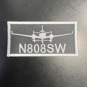 May include: A white embroidered patch with a small airplane and the text "N808SW" on a black background.