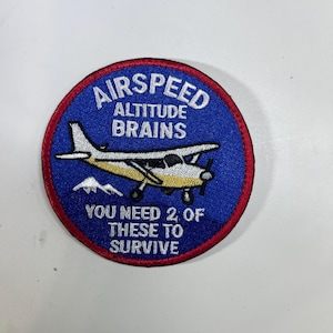 May include: Embroidered patch with a blue background and a red border. The patch features a yellow and white airplane, mountains, and the text "AIRSPEED ALTITUDE BRAINS YOU NEED 2 OF THESE TO SURVIVE."