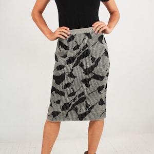 May include: A woman wearing a black turtleneck top and a grey and black patterned knitted skirt. She is wearing black ankle boots.
