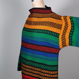 May include: A colorful striped sweater with a high neck and long sleeves. The sweater is made of a thick, textured fabric and features a variety of colors, including red, orange, yellow, green, blue, and black.