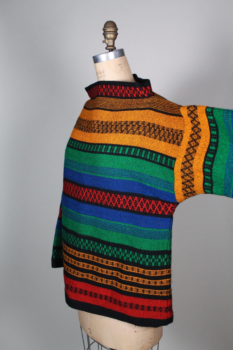 May include: A colorful striped sweater with a high neck and long sleeves. The sweater is made of a thick, textured fabric and features a variety of colors, including red, orange, yellow, green, blue, and black.