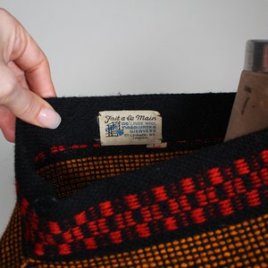 May include: Black and orange woven sweater with a red stripe and a label that reads "Fait a la Main 100% Pure Wool Mascouche Weavers St. Leonard, N.E. Canada."