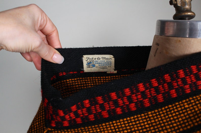 May include: Black and orange woven sweater with a red stripe and a label that reads "Fait a la Main 100% Pure Wool Mascouche Weavers St. Leonard, N.E. Canada."