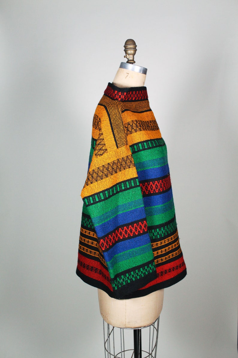 May include: A colorful striped sweater with a high neck and long sleeves. The sweater is made of a thick, textured yarn and features a variety of colors, including red, orange, yellow, green, blue, and black.