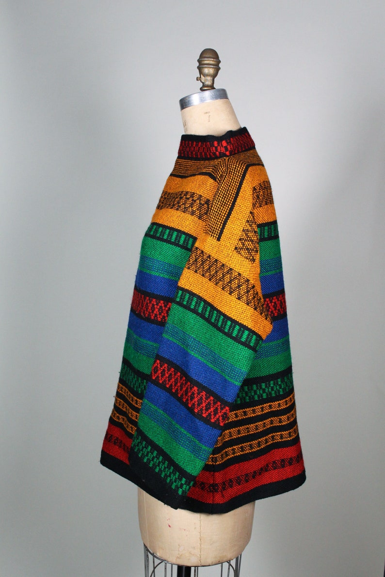 May include: A colorful striped sweater with a high neck. The sweater is made of a thick knit fabric and features a variety of colors, including red, orange, yellow, green, blue, and black.