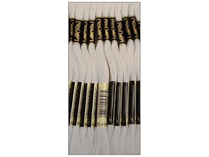 May include: A bundle of 25 white embroidery floss spools with gold and black labels. The labels read "DMC" and "BLANC".
