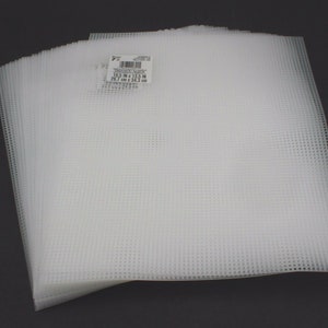 Może przedstawiać: Stos białych plastikowych pł&oacute;cien o wymiarach 26,7 cm x 34,3 cm. Etykieta zawiera napis "7" count plastic canvas, 10.5 in x 13.5 in, 26.7 cm x 34.3 cm.