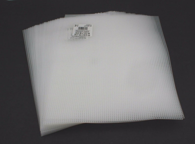 Może przedstawiać: Stos białych plastikowych pł&oacute;cien o wymiarach 26,7 cm x 34,3 cm. Etykieta zawiera napis "7" count plastic canvas, 10.5 in x 13.5 in, 26.7 cm x 34.3 cm.