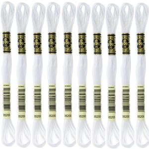 May include: A collection of twelve white embroidery floss skeins. Each skein has a gold and black label with the number "25" and the brand name "DMC". The bottom of each label displays the number "85200".