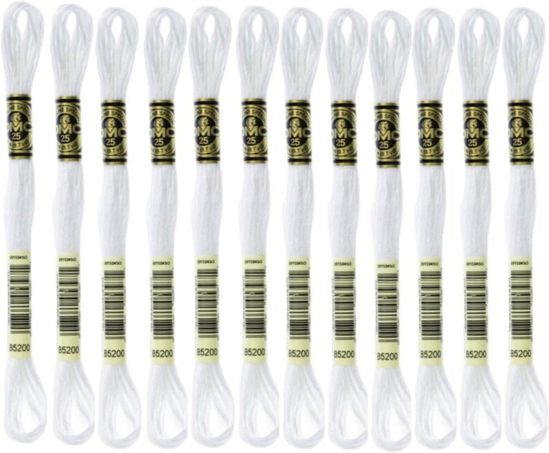 May include: A collection of twelve white embroidery floss skeins. Each skein has a gold and black label with the number "25" and the brand name "DMC". The bottom of each label displays the number "85200".