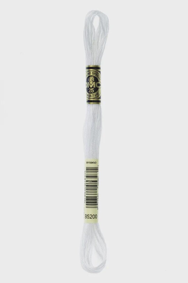 May include: A white DMC embroidery floss skein. The label reads "DMC 25" and "8.7 yd". The barcode and the code "B5200" are also visible. This craft supply is used for embroidery, cross-stitch, and other needlework projects.