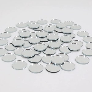 May include: A large pile of round, silver mirror tiles. The tiles are scattered on a white surface.