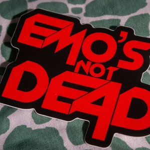 Op de afbeelding: Zwarte en rode sticker met de tekst "Emo's Not Dead" in een vet, gestileerd lettertype.