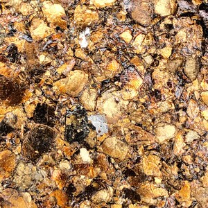 May include: Close-up of a textured surface with a gold and brown color scheme. The surface is made up of small, irregular pieces that resemble broken pieces of gold leaf.