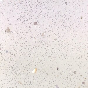 May include: Close-up of a white surface with small, speckled flecks of various colors and shapes.