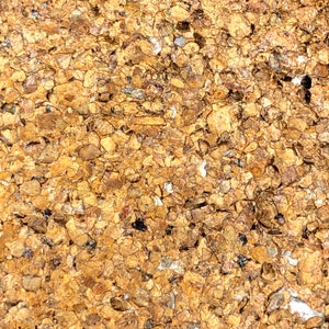May include: Close-up of a textured surface made of small, irregularly shaped, golden brown pieces. The surface has a rough, uneven texture.