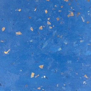 May include: A close-up of a blue surface with small, scattered flecks of gold and silver. The surface has a textured, slightly rough appearance.