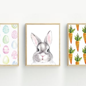 May include: Three framed watercolor prints with Easter themes. The first print features a pattern of colorful Easter eggs. The second print shows a gray bunny rabbit with pink ears. The third print features a pattern of orange carrots with green tops.