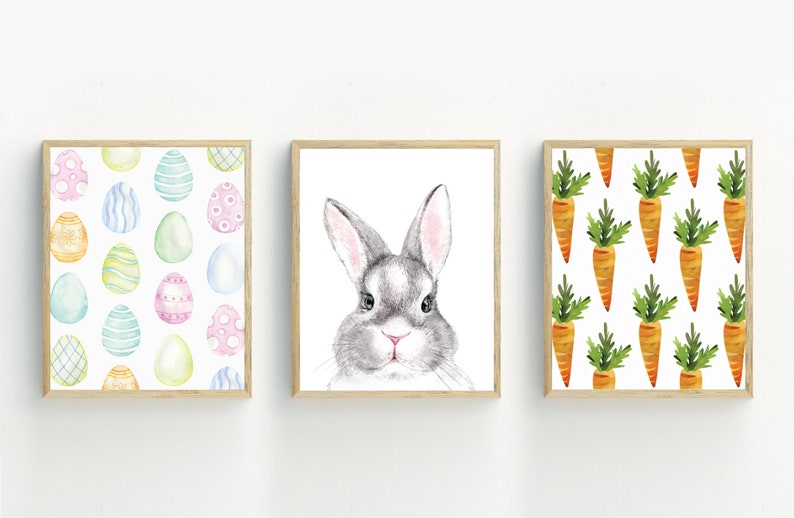 May include: Three framed watercolor prints with Easter themes. The first print features a pattern of colorful Easter eggs. The second print shows a gray bunny rabbit with pink ears. The third print features a pattern of orange carrots with green tops.