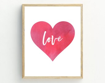 May include: A framed print with a watercolor heart in shades of pink and red. The word "love" is written in white script inside the heart.