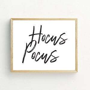 May include: A framed print with the words "Hocus Pocus" written in black brush script on a white background.