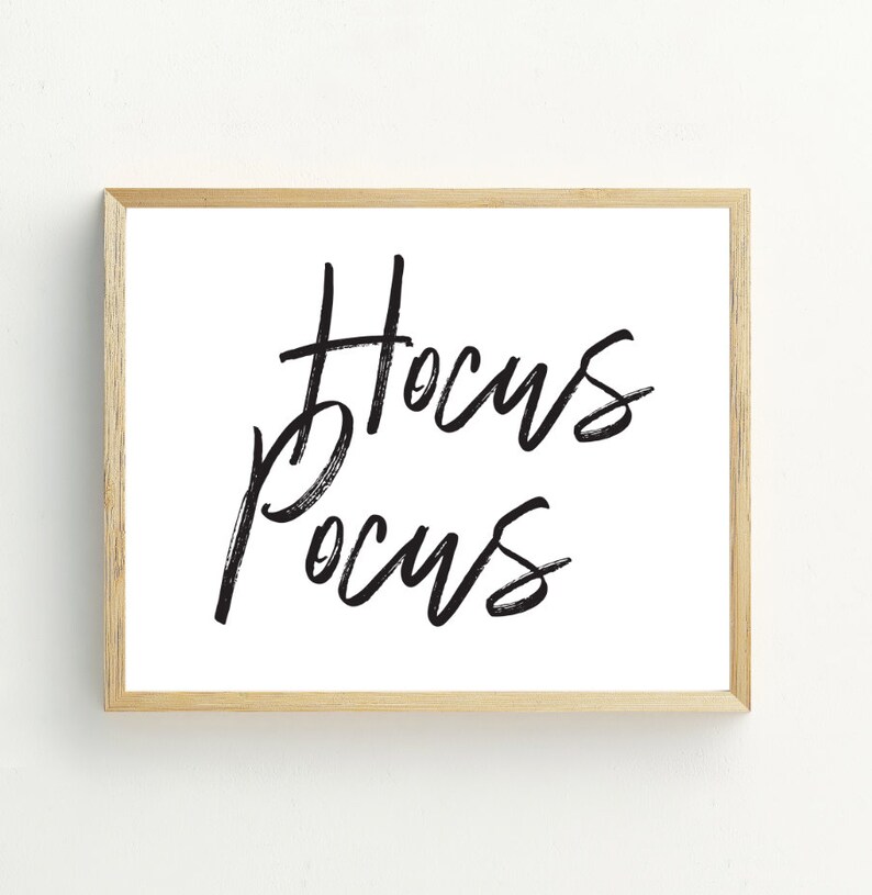 May include: A framed print with the words "Hocus Pocus" written in black brush script on a white background.