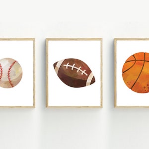 May include: Three framed prints of watercolor illustrations of sports balls. The prints feature a baseball, a football, and a basketball.
