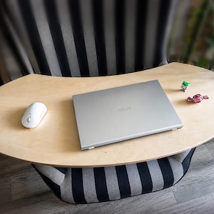 Puede incluir: Un escritorio de madera clara para portátil con un portátil plateado, un ratón blanco y pequeños objetos decorativos. El escritorio está sobre un cojín a rayas. El portátil tiene la marca "ASUS".