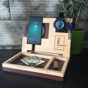 May include: Wooden organizer with compartments for a phone, watch, keys, and other small items. The organizer has a charging pad for a phone and the text "CLEVERBOARD" is engraved on the front.