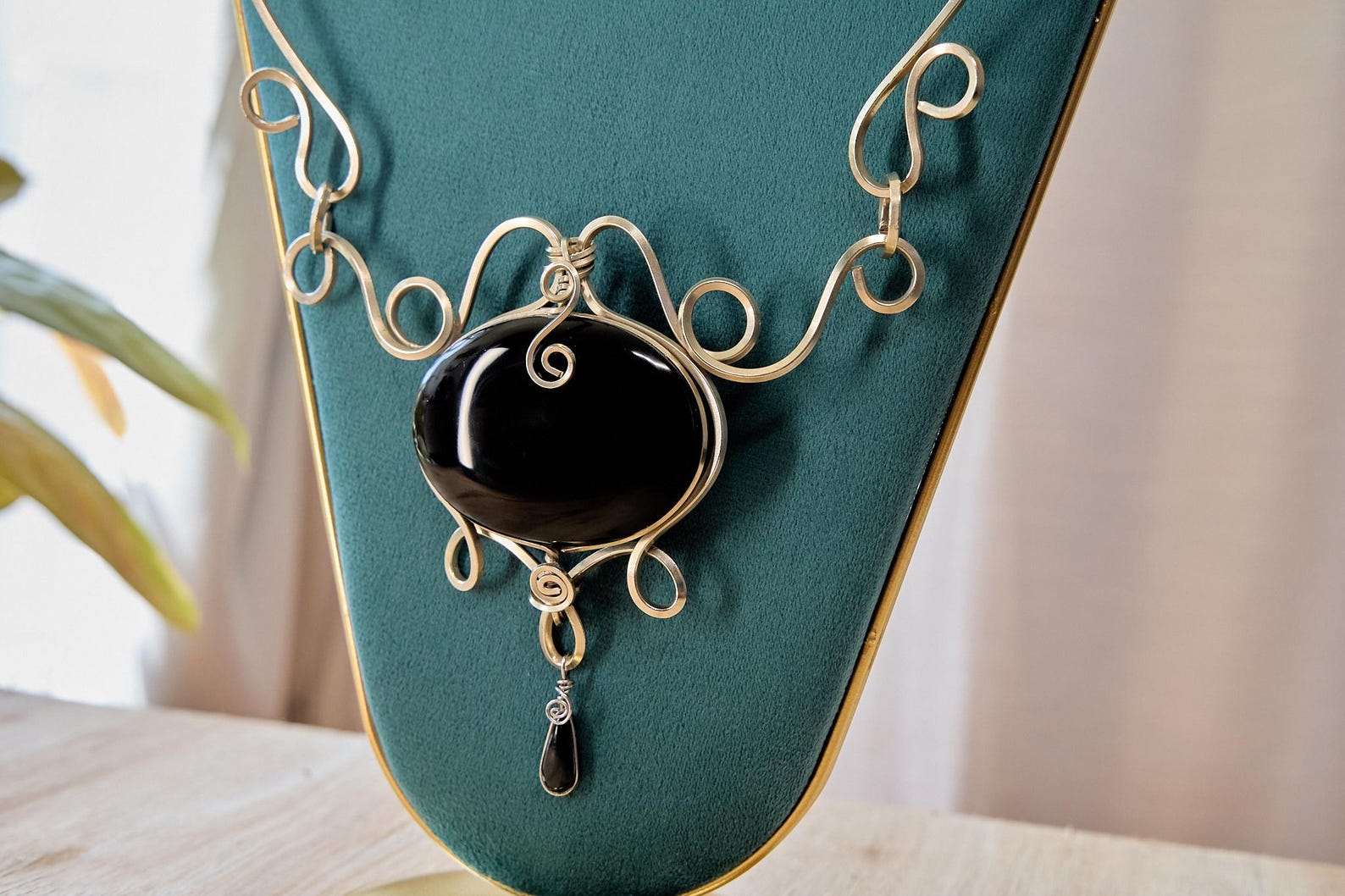 Close-up of handmade Mexican black obsidian necklace with silver wire scroll design on a green display stand.