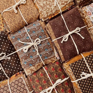 May include: A collection of folded fabric squares tied with white string, featuring various patterns including polka dots, floral motifs, paisley, and geometric shapes in shades of brown, tan, cream, blue, and red.
