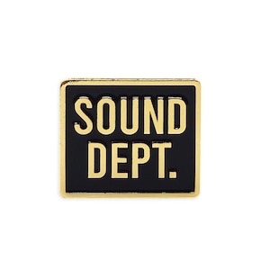 Puede incluir: Un pin cuadrado con fondo negro y borde dorado. El pin presenta las palabras "SOUND DEPT." en letras doradas. El diseño es simple y audaz.