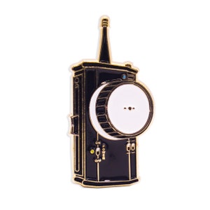 May include: A black and gold enamel pin shaped like a vintage camera with a white lens and a small blue detail. The pin has a gold 'ON' and 'OFF' switch and a gold 'POWER' button.