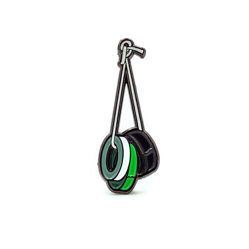 May include: A black, green and white enamel pin of three rolls of tape hanging from a string.