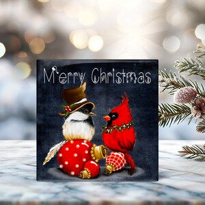 May include: A black and white Christmas ornament with a bird wearing a top hat and a red cardinal. The ornament has the text "Merry Christmas" on it.