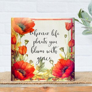 May include: Square art print featuring vibrant red poppy flowers and the quote "Wherever life plants you bloom with grace." The floral design includes green leaves and buds. The artwork is set against a cream background with a red border.