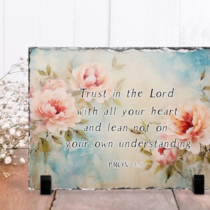 May include: A rectangular slate plaque featuring a floral design with pink and peach peonies. The text "Trust in the Lord with all your heart and lean not on your own understanding PROV 3:5" is displayed. The plaque is supported by a black stand.